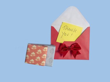 Sarı teşekkür notu kırmızı zarfa ve kırmızı fiyonk mavi arka planda hediye kutusuna.