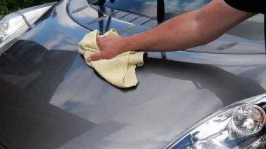 Arabanın kaputunu yumuşak bir bezle cilalayan bir adamın yakın çekimi.