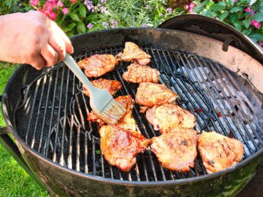 Sıcak bir yaz akşamında sıcak kömürlerin üzerinde tavuk butlarını salamura ile fırçalamak.