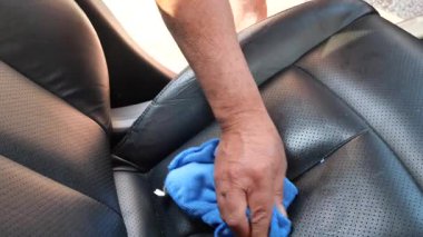 Deri koltuğu nemli yumuşak bir bezle temizleyen adamın yakın çekimi toz ve tozu temizliyor.