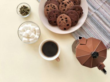 Gayzer kahve makinesi, bir fincan kahve, şeker, kakule, kurabiye ve mutfak havlusu..