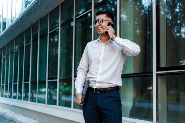 Beyaz gömlek giyen bir adam telefonda bir konuşmayla meşgul. Cihaz aracılığıyla iletişim kurarken odaklanmış ve özenli görünüyor..