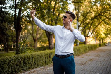 Beyaz gömlekli ve mavi pantolonlu bir adam elinde bir cep telefonu tutuyor..