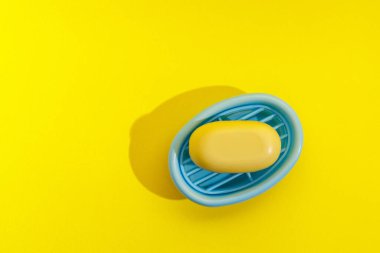 Sarı bir sabun, parlak sarı bir yüzey üzerinde mavi bir kapta durur..