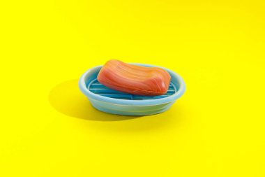 Tek bir kalıp sabun sarı arkaplanda mavi bir kapta oturur..