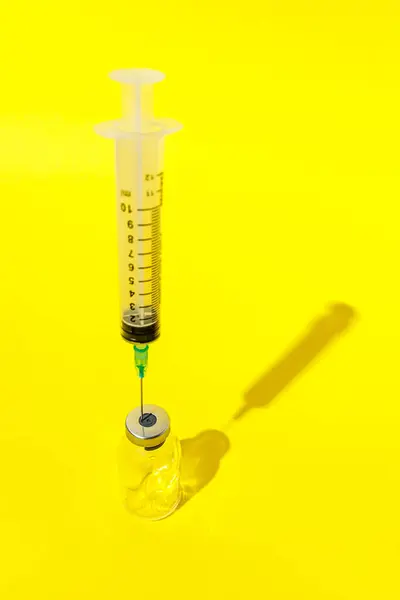 stock image A clear syringe with a green needle is inserted into the top of a clear glass vial on a bright yellow background.