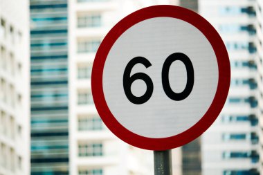 Saatte 60 kilometre hız limitini gösteren kırmızı ve beyaz hız limiti işareti modern bir binanın önündeki direğe monte edilir..