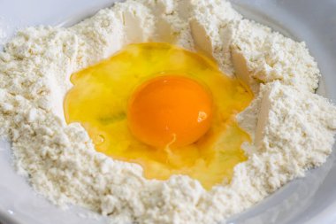 Tek bir yumurta sarısı, beyaz bir kâse üzerindeki beyaz un halkasesiyle çevrili bir un kuyusunda dinlenir..