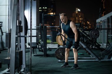 Siyah spor elbiseli bir adam geceleri spor salonundaki bir kablo makinesinde çalışıyor..