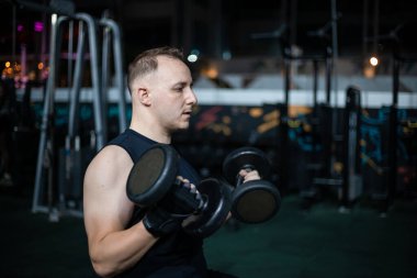 Bir adam loş bir spor salonunda çalışırken ağırlık kaldırır..