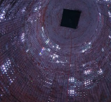 Fotoğraf, sayısız küçük ışıkla aydınlatılmış bir tuğla bacanın içini gösteriyor. Aşağıdan görünüm, tuğla dokusu ve çok sayıda ışık noktası.