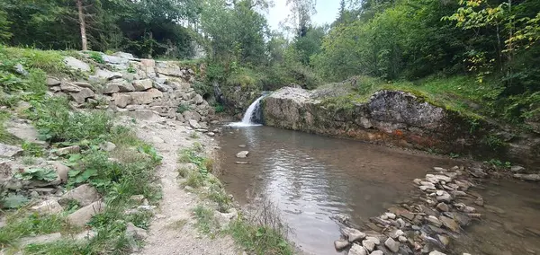 Pieniny 'deki alışveriş merkezi şelalesi, kayaların ve ağaçların arasına saklanmış. Su kayalık bir gölete düşer. Taş yığını ve orman yerleşimi huzurlu bir manzara yaratır..
