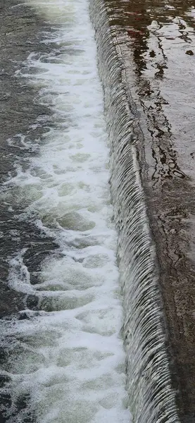 Fotoğraf nehirdeki su basamaklarının yakın çekimini gösteriyor. Görünür köpüklü su dökülüyor. Su ve betonun detaylı dokusu.