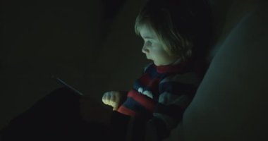 Çocuk geceleri dijital tabletin tadını çıkarıyor. Oturma odasında, kanepede oturuyor.