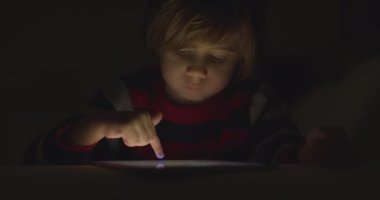 Çocuk geceleri dijital tabletin tadını çıkarıyor. Oturma odasında, kanepede oturuyor.