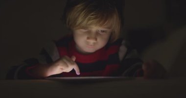Çocuk geceleri dijital tabletin tadını çıkarıyor. Oturma odasında, kanepede oturuyor.
