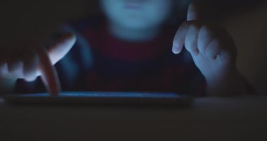 Çocuk geceleri dijital tabletin tadını çıkarıyor. Oturma odasında, kanepede oturuyor.