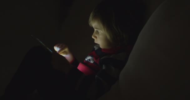 男の子は夜にデジタルタブレットを楽しんで ソファーに座ってリビングルームで — ストック動画