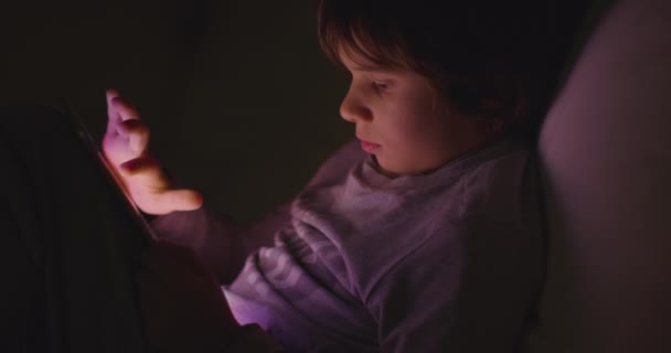 男の子は夜にデジタルタブレットを楽しんで ソファーに座ってリビングルームで — ストック動画