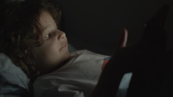 男の子は夜にデジタルタブレットを楽しんで ソファーに座って リビングルームで 暗闇の中で — ストック動画