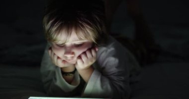 Çocuk geceleri dijital tabletin tadını çıkarıyor, kanepede oturuyor, oturma odasında, karanlıkta.
