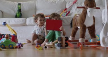 Kanepede tablet kullanan mutlu çocuk. Sosyal medyayı kaydırmak, internette sörf yapmak, evde eğlenmek. Müzik dinleyip, video izlerken bir yaşındaki kardeşi oyuncaklarla oynuyor.