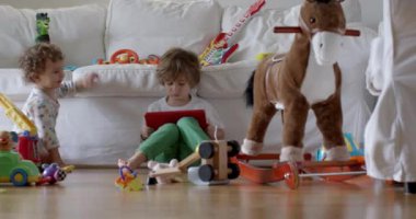 Kanepede tablet kullanan mutlu çocuk. Sosyal medyayı kaydırmak, internette sörf yapmak, evde eğlenmek. Müzik dinleyip, video izlerken bir yaşındaki kardeşi oyuncaklarla oynuyor.