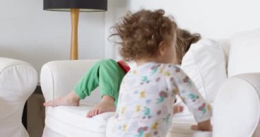 Kanepede tablet kullanan mutlu çocuk. Sosyal medyayı kaydırmak, internette sörf yapmak, evde eğlenmek. Müzik dinleyip, video izlerken bir yaşındaki kardeşi oyuncaklarla oynuyor.