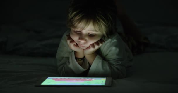 男の子は夜にデジタルタブレットを楽しんで ソファーに座って リビングルームで 暗闇の中で — ストック動画