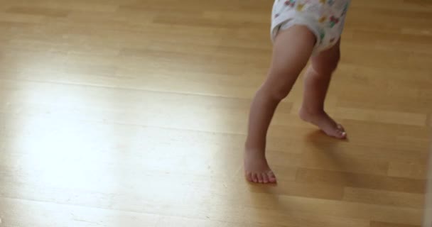 赤ちゃんは木製の床で最初の一歩を踏み出し 子供は歩くことを学んでおり 冷蔵庫を開けています ハッピーファミリーコンセプト — ストック動画