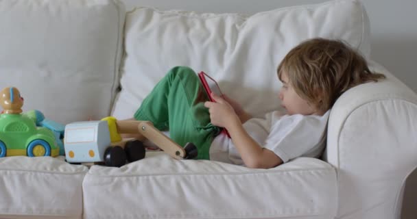 Gyermek Feküdt Egy Fehér Kanapén Egy Digitális Tabletta Egy Szobában — Stock videók