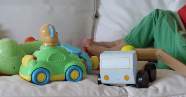 おもちゃでいっぱいの部屋で デジタルタブレットを使用して白いソファーに横たわっている若い子供 — ストック動画