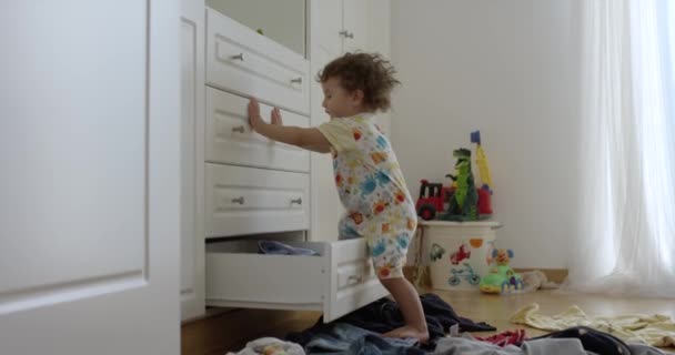 歳の男の子はクローゼットから服を投げ出す 混乱した寝室 遊んで 屋内で楽しんでいます 低い角度ビュー — ストック動画