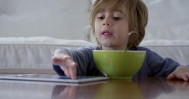 Üç yaşında bir çocuk kahvaltısını yaparken dijital tablet kullanıyor.