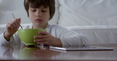 Üç yaşında bir çocuk kahvaltısını yaparken dijital tablet kullanıyor.