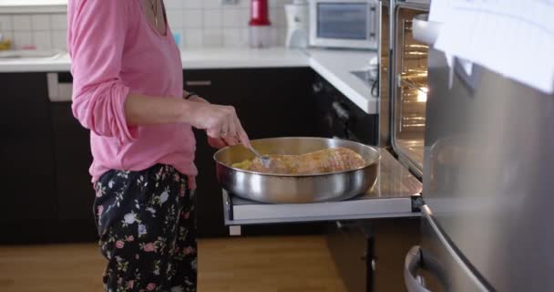 オーブンで食事を準備している女性は 赤ちゃんの男の子を抱えている間 昼間は明るいホームキッチンで — ストック動画