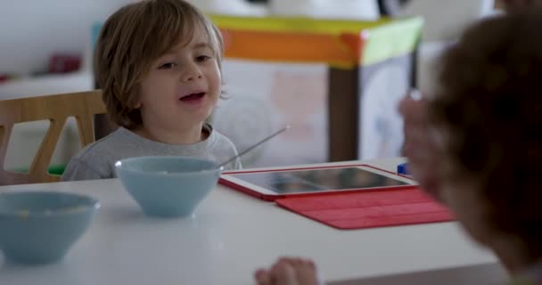 男の子は彼の前にデジタルタブレットで朝食のテーブルに座っている間話します — ストック動画