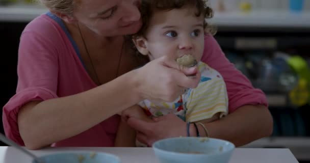 男の子は彼の目の前にデジタルタブレットで朝食のテーブルに座っている間 母親は赤ちゃんに餌を与えています — ストック動画