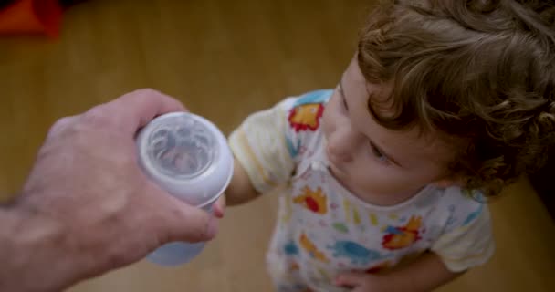 一个男孩 一头卷曲的头发 看着一只成人的手拿着瓶子 父亲拿着瓶子 — 图库视频影像