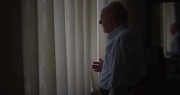 Старший Чоловік Стоїть Біля Вікна Дивлячись Через Штори Втрачені Думці — стокове відео