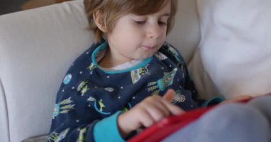 Bir bebek, dijital tablet kullanarak koltukta dinlenirken oyuncakla oynamaktan zevk alır..