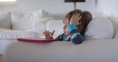 Bir bebek, dijital tablet kullanarak koltukta dinlenirken oyuncakla oynamaktan zevk alır..