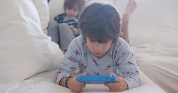 Duas Crianças Focadas Dispositivo Jogo Portátil Enquanto Estavam Deitadas Sofá — Vídeo de Stock