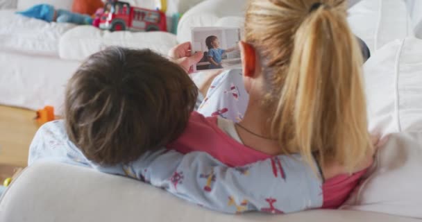 年轻的母亲带着孩子躺在客厅的沙发上看打印的全家福 — 图库视频影像