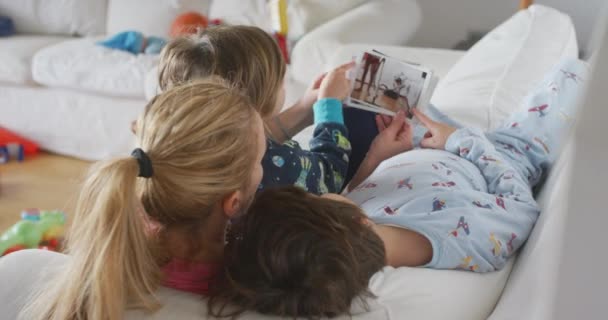 年轻的母亲带着孩子躺在客厅的沙发上看打印的全家福 — 图库视频影像