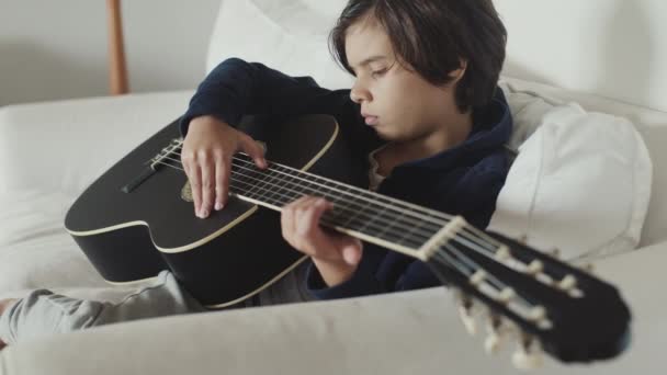 Симпатичний Молодий Хлопчик Коричневим Волоссям Сидить Дивані Нанизуючи Гітару Концентрацією — стокове відео