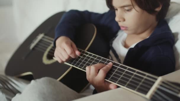 Aranyos Fiatal Fiú Barna Hajjal Kanapén Szvingelve Egy Gitárt Koncentrációval — Stock videók