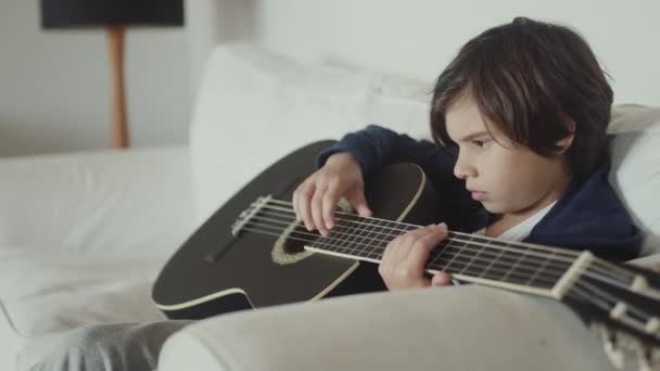Cute Young Boy Brown Hair Seated Couch Strumming Guitar Concentration — Stock Video