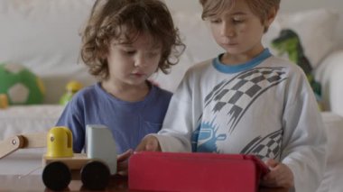 Çocuklar oyuncakları keşfediyor ve öğreniyor, birlikte eğlenceli bir aktiviteye giriyorlar, bu sırada parlak, modern bir oturma odasında dijital tablet kullanıyorlar..