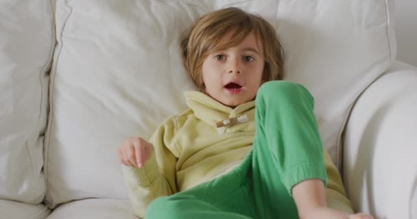 Niño Pequeño Sorprendido Mientras Descansa Sofá Con Pijama Verde Brillante — Vídeos de Stock